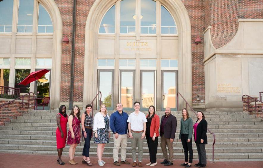 staff members from the office of academic advising. st和ing in front of an academic building. team of 11 advisors.