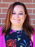 A photo of Kara Taczak, a woman with shoulder-length auburn hair smiling at the camera